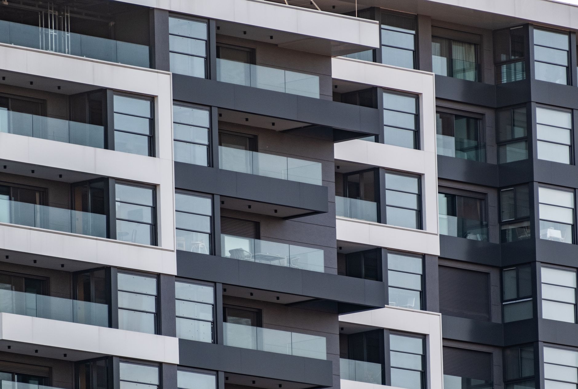 Façade d’un immeuble moderne avec balcons à garde-corps en verre, panneaux blancs et gris foncé et rangées de fenêtres.